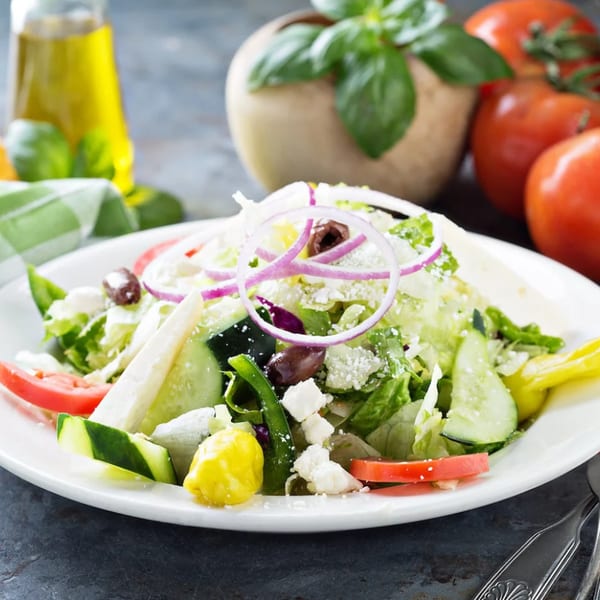 A fresh Greek salad with lettuce, tomatoes, cucumbers, olives, feta, and red onion.