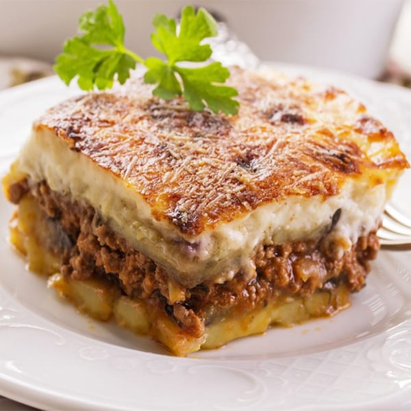 A close-up of a Greek moussaka with layers of meat, potatoes, and béchamel sauce, garnished with parsley.