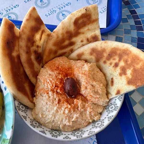 Hummus topped with paprika and an olive, surrounded by warm pita bread on a patterned plate.