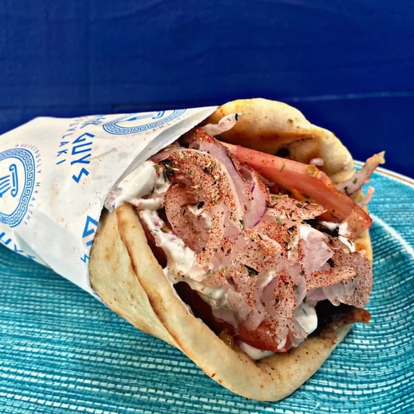 A Greek Guys Souvlaki gyro, filled with meat, tomatoes, onions, and tzatziki, on a blue plate.