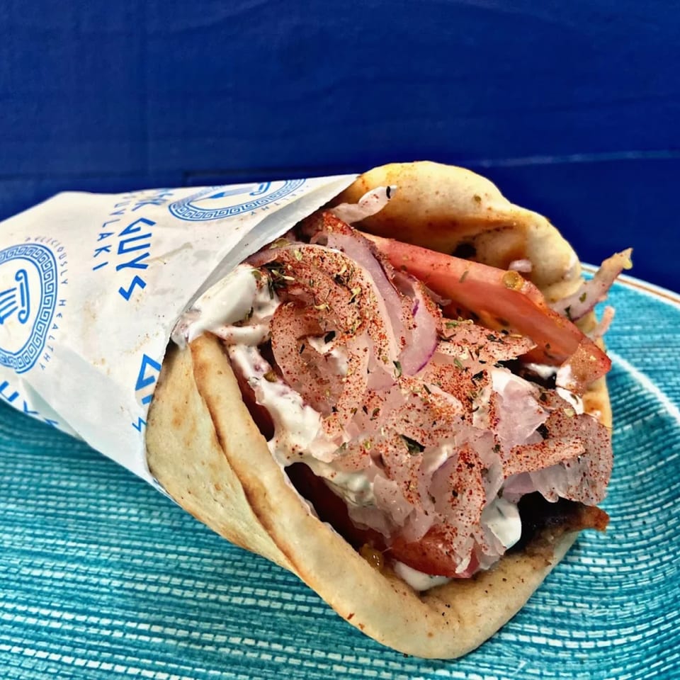 A Greek Guys Souvlaki gyro, filled with meat, tomatoes, onions, and tzatziki, on a blue plate.
