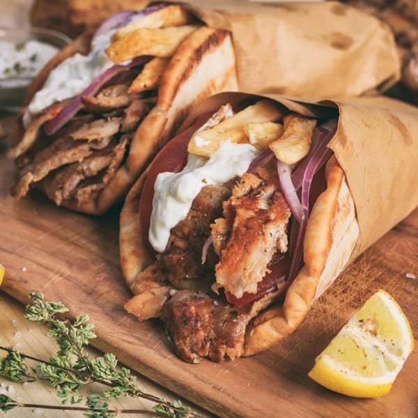 Two Greek Guys Souvlaki gyros with meat, fries, red onion, and tzatziki on a wooden board.
