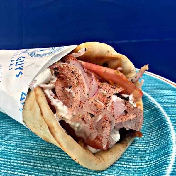 A Greek Guys Souvlaki gyro, filled with meat, onions, tomatoes, and sauce, on a blue plate.